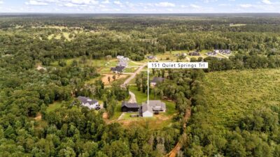 An aerial view of 151 Quiet Springs Trail, showing the home and detached garage building on their cul-de-sac homesite, surrounded by mature trees within Peach Creek Farms.