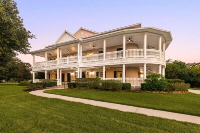 Two-story Southern-style home in Old Katy, TX with wraparound porches on both levels, surrounded by mature trees on a 2.46-acre lot