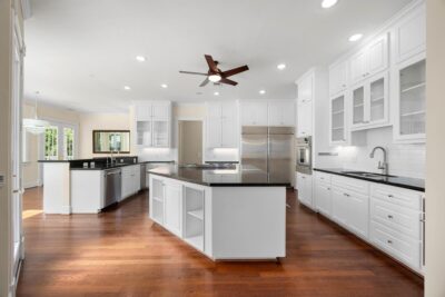Large chef’s kitchen featuring two oversized islands, a commercial-style refrigerator/freezer, dual wall ovens, glass-front cabinetry, and rich granite countertops.