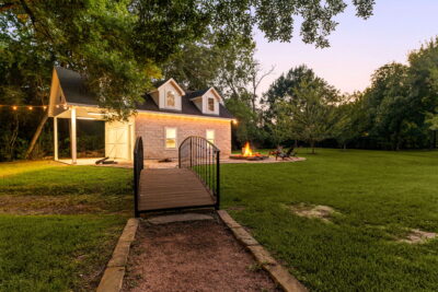 Houston fall home exterior with warm lighting, a spacious lawn, and inviting outdoor gathering area at dusk.