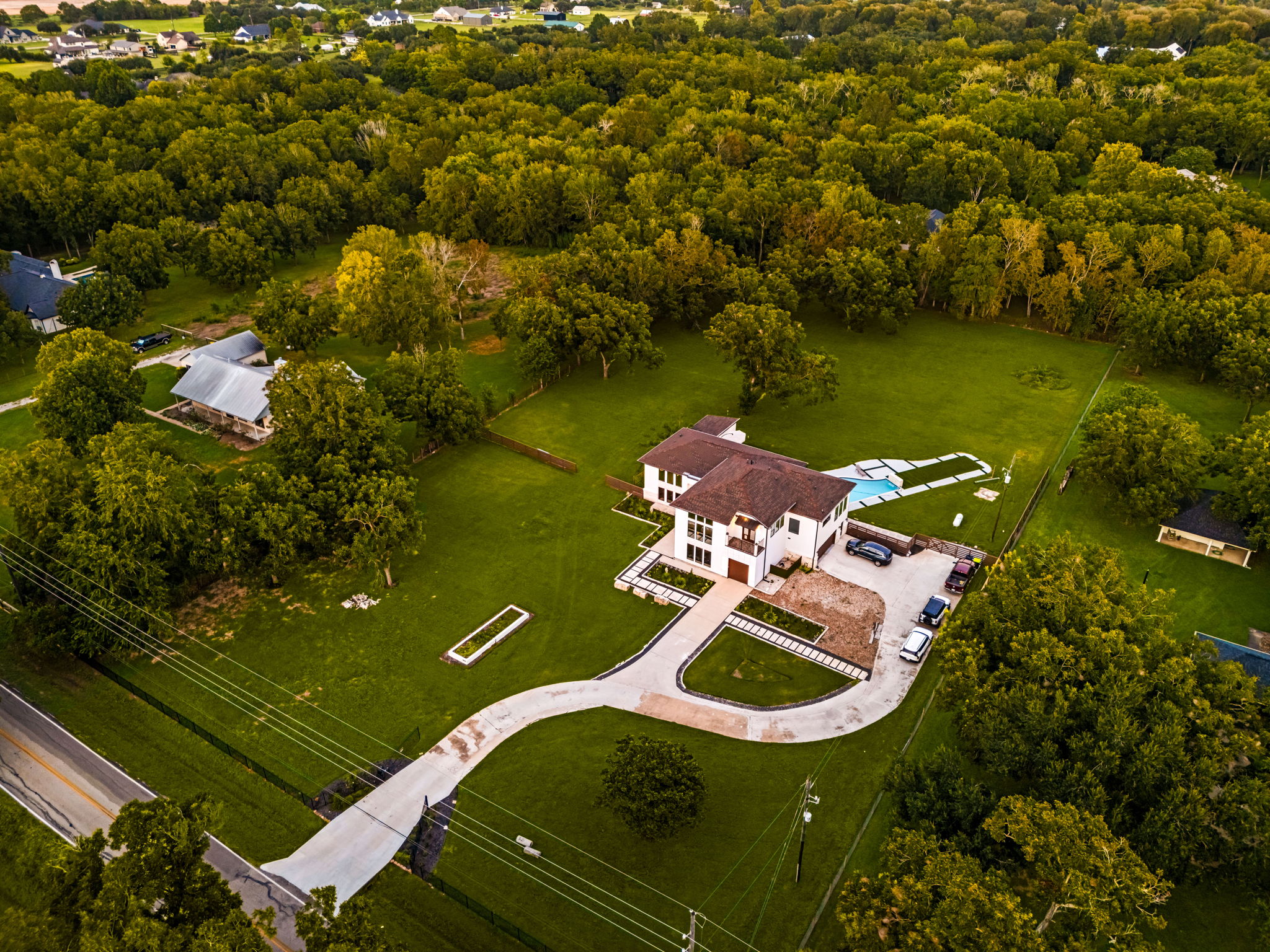 Aerial view of a modern two-story Fulshear home on an acreage lot with a pool, a curved driveway, and mature trees, showing the Fulshear real estate market