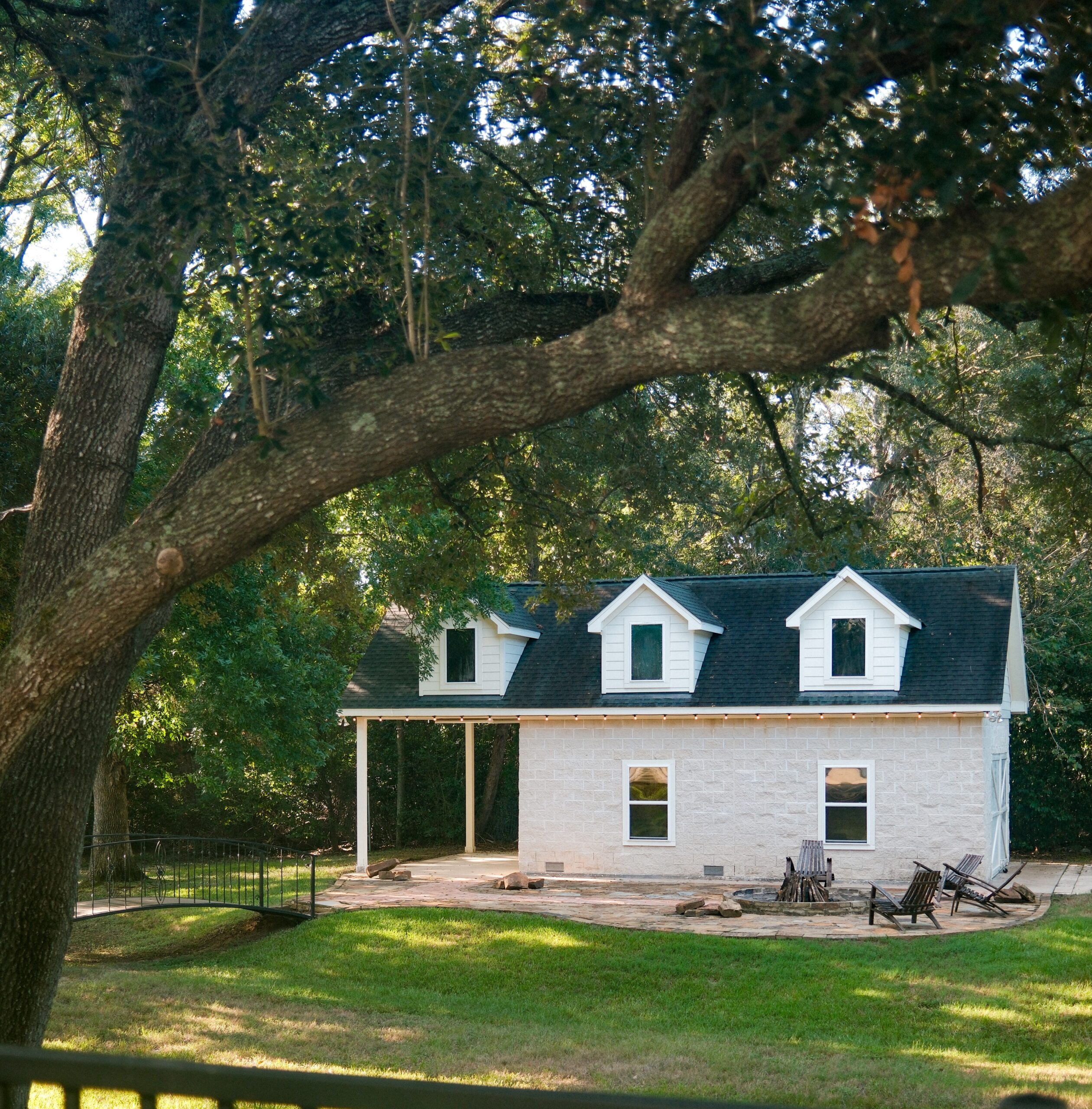 Katy homes for sale with outdoor living, including a white dormered cottage, stone fire pit patio, and mature live oak