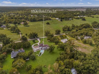 Aerial view of a home for sale in Fulshear on 2.66 acres at 6830 Bois D’Arc Lane, showing the curved driveway, pool, mature trees and surrounding open pastures